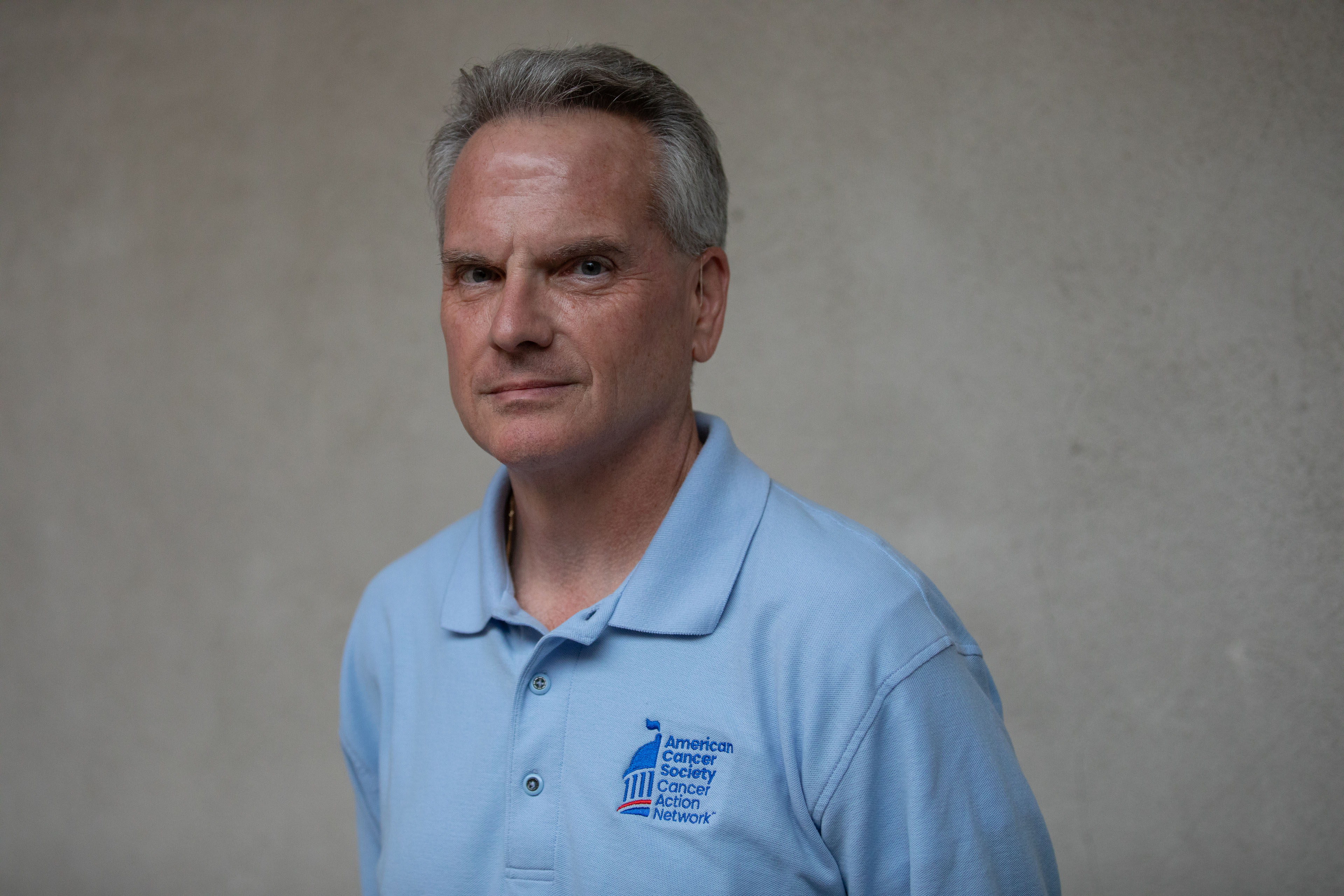 Common-ground-cancer-01 A portrait of an older man wearing a blue shirt against a grey background.