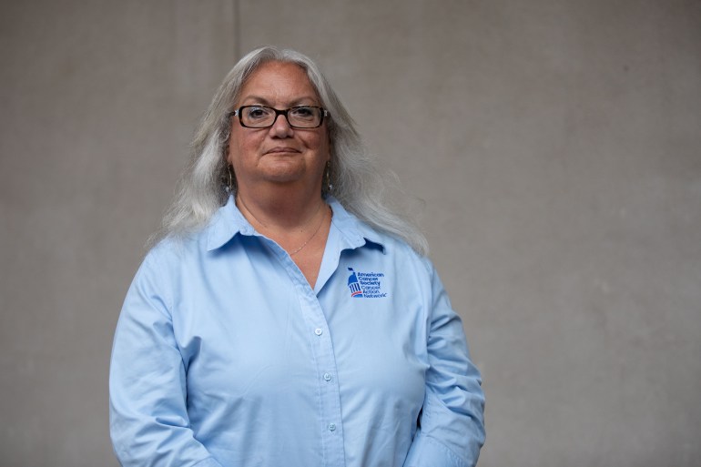 Common-ground-cancer-02 A portrait of an older woman wearing a blue shirt standing against a gray background.