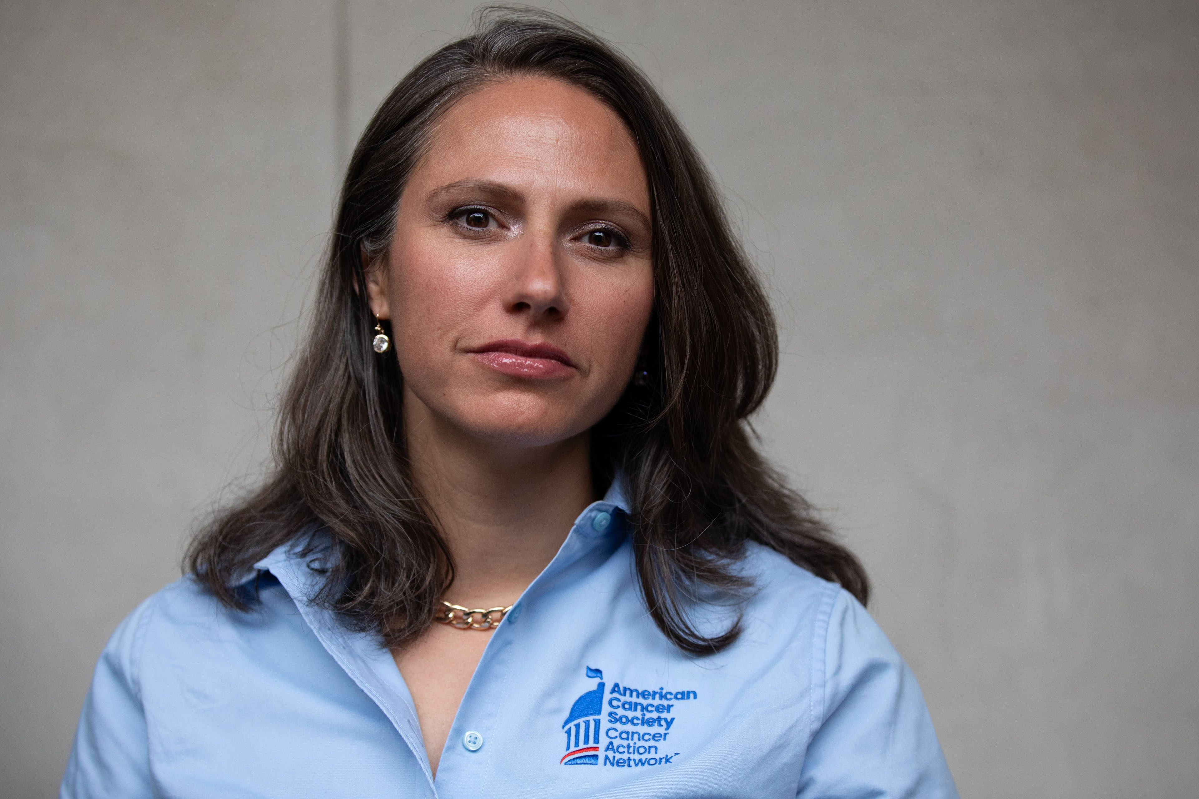 Common-ground-cancer-03 A portrait of a woman wearing a blue shirt standing against a gray background.