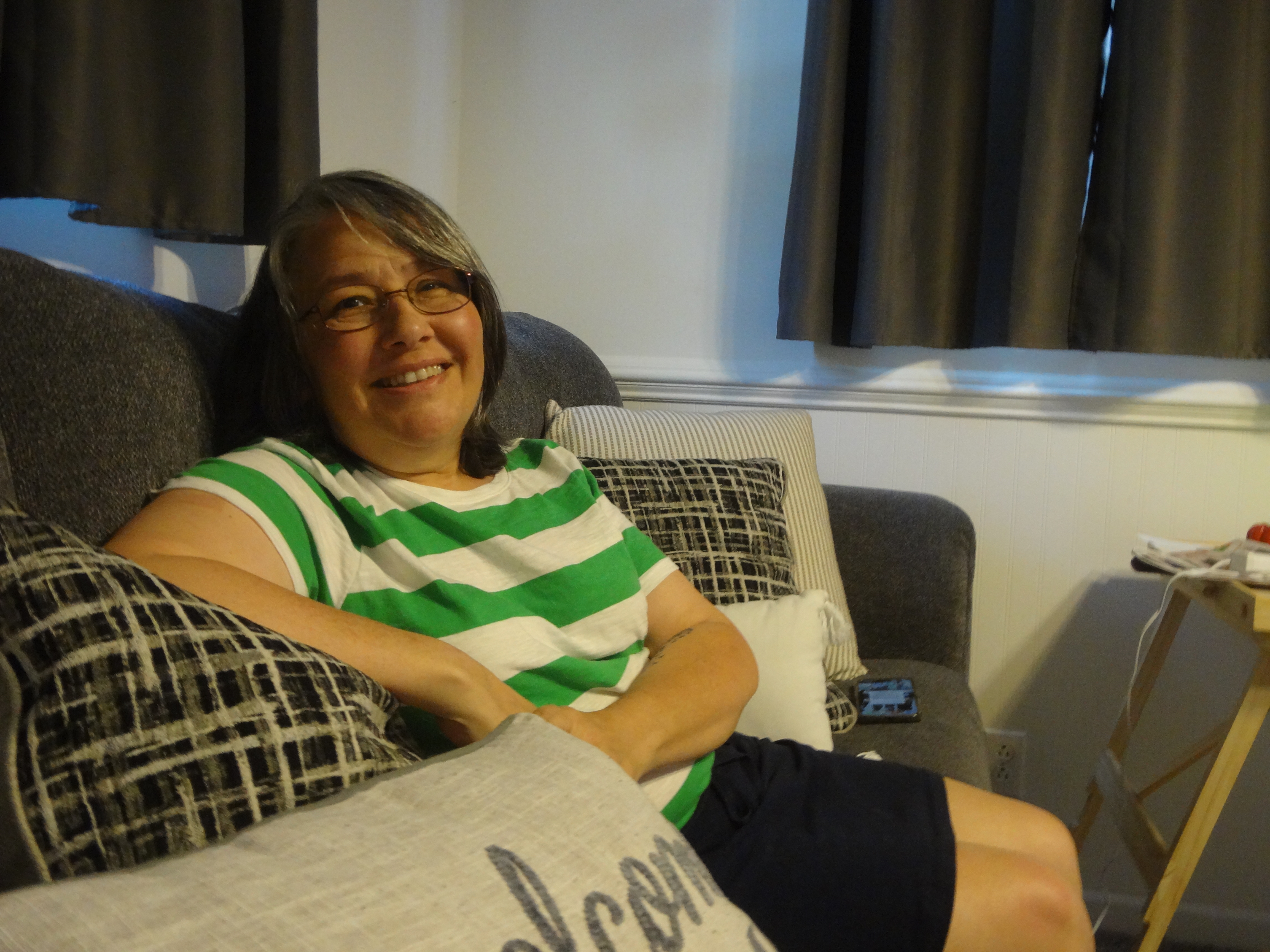 Subrenda-Huff A woman with glasses and a green and white striped tshirt sits on a couch
